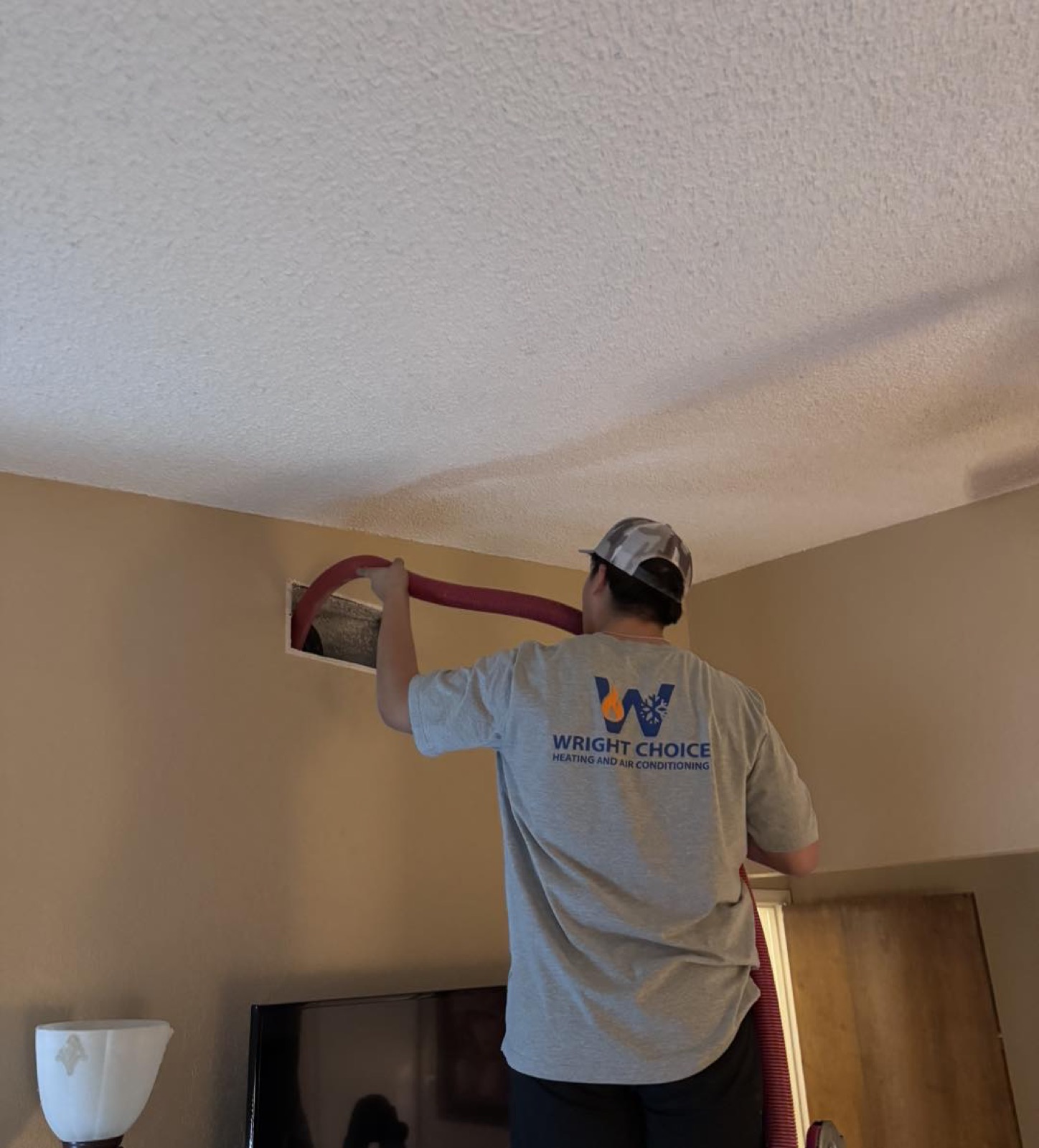 Wright Choice technician cleaning a ceiling air duct register inside an Abilene, TX home