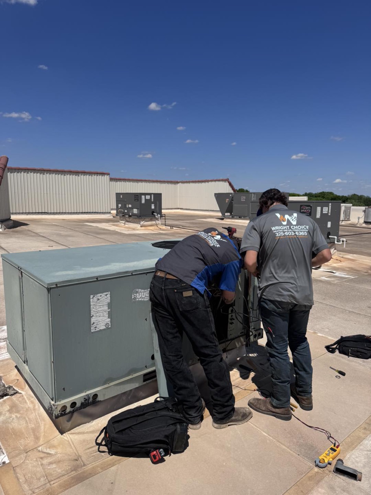 Two Wright Choice technicians servicing a Ruud rooftop package unit on a commercial roof in West Texas